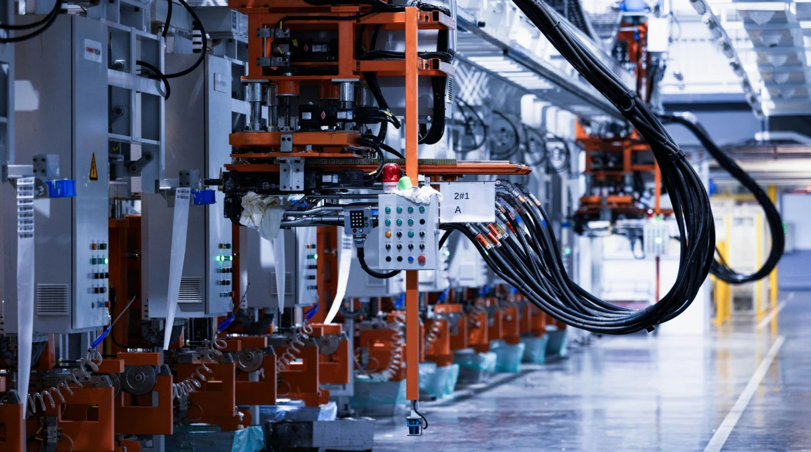 Orange robotic assembly stations with cable bundles and control panels lining an automated production line