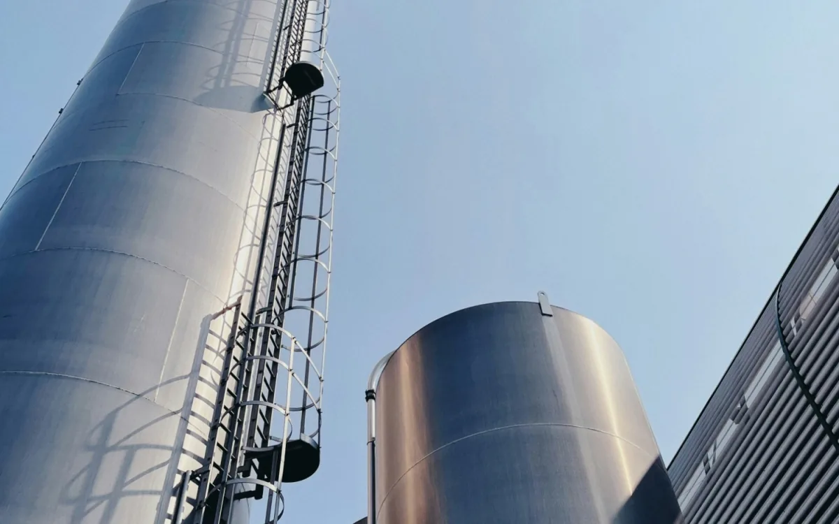 Tall steel silos with caged access ladders against a clear sky at an industrial plant