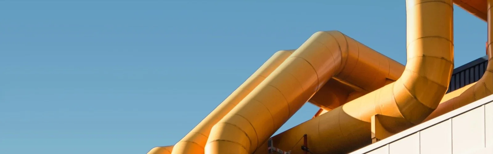 Insulated ducting running along the roofline of an industrial plant against a clear sky